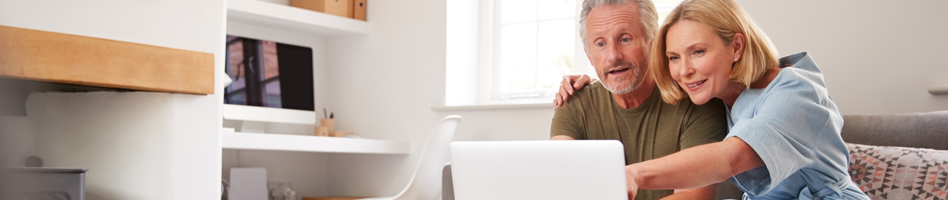 Ouder echtpaar zit thuis op de bank en gebruikt samen een laptop